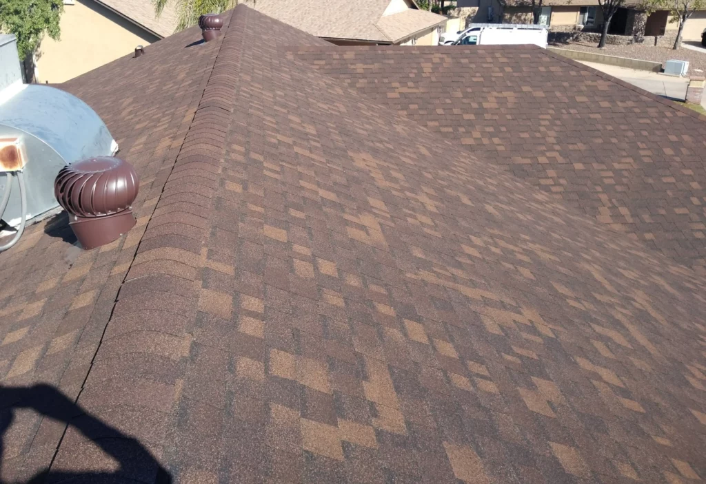 Close-up view of a residential shingle roof with brown and tan patterned shingles in Arizona, including ventilation components.