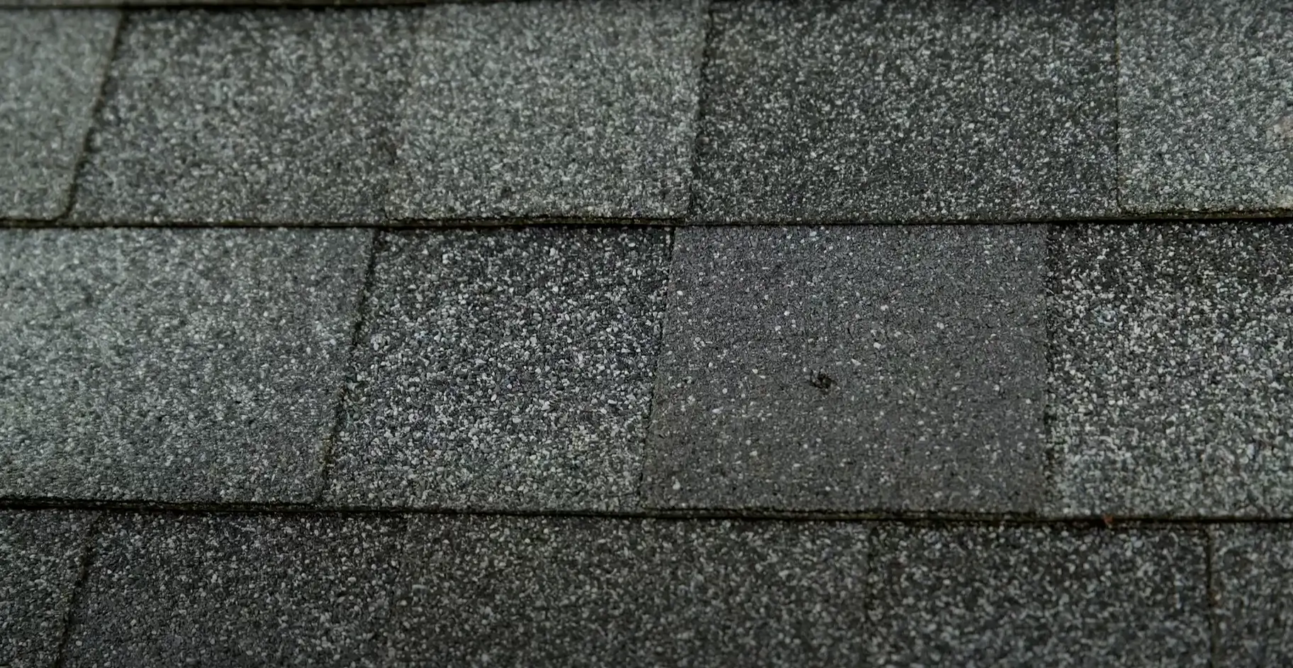 Close-up of dark gray asphalt roofing shingles with a textured, granular surface, showcasing the pattern and structure of traditional roofing materials.