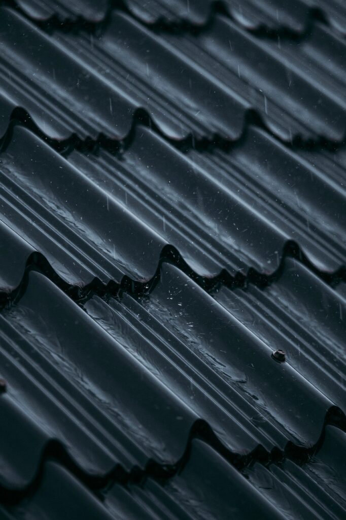Close-up of a dark, wet tile roof during rainfall, showing water droplets sliding across the surface—highlighting the importance of proper waterproofing and leak prevention.