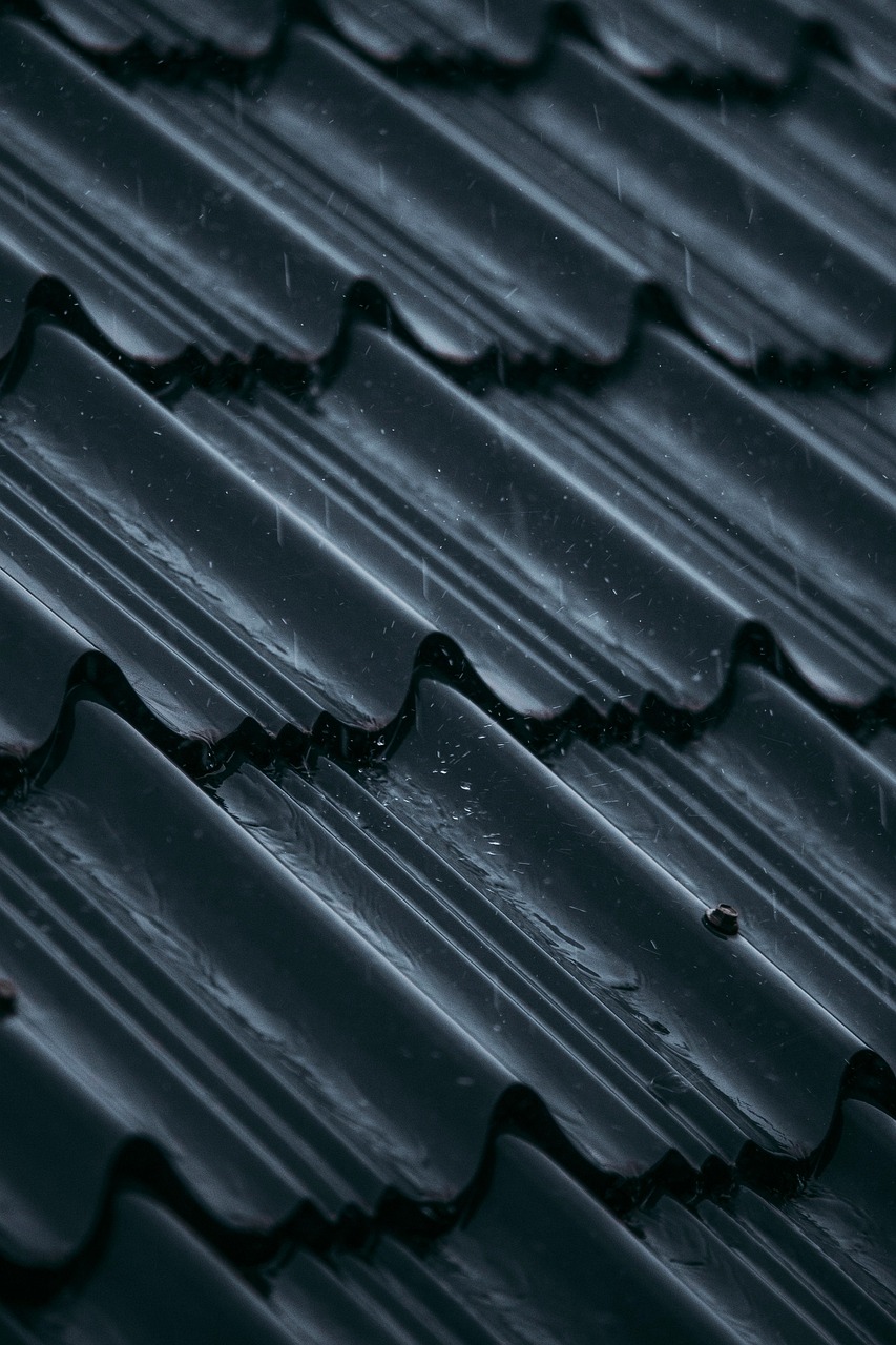 Close-up of a dark, wet tile roof during rainfall, showing water droplets sliding across the surface—highlighting the importance of proper waterproofing and leak prevention.