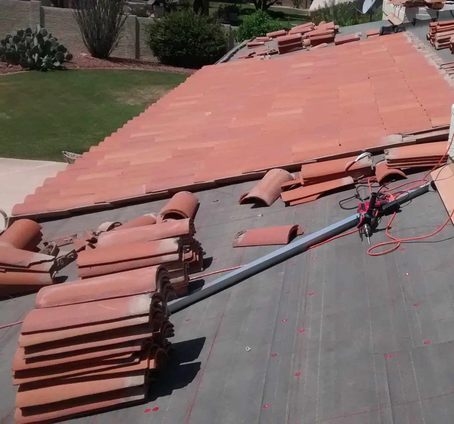 Arizona roof under construction with reddish clay tiles being installed in neat rows, showing tile stacks, underlayment, and roofing tools on a residential rooftop.