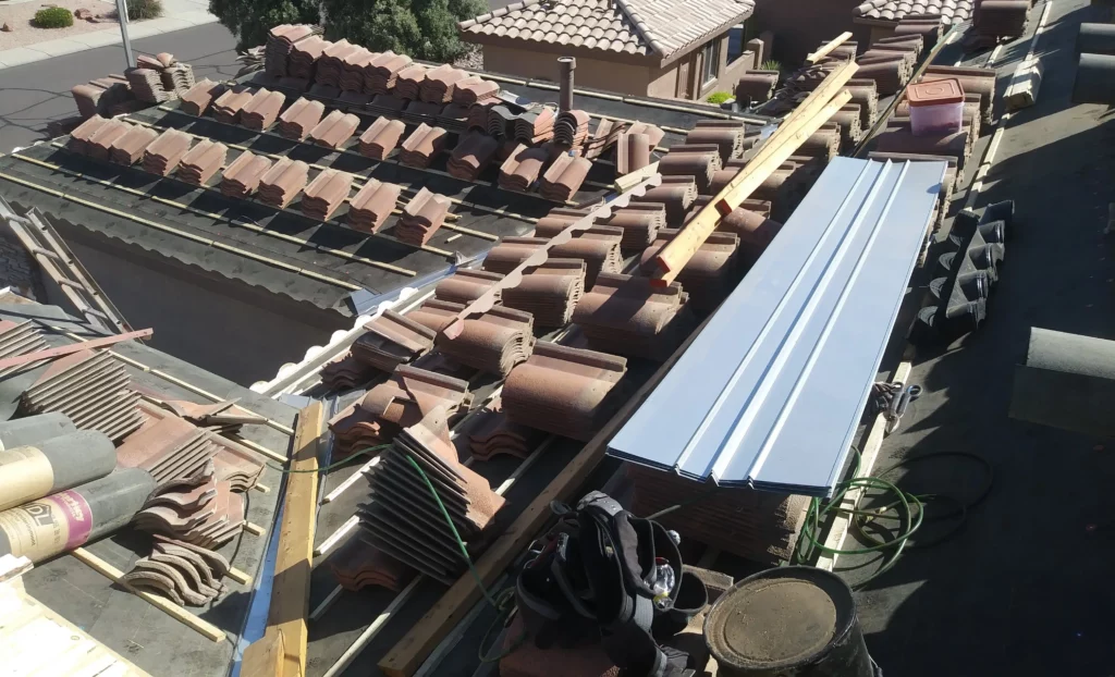 Arizona Roof under construction with stacks of clay tiles, underlayment, metal flashing, and various roofing tools and materials laid out for installation.