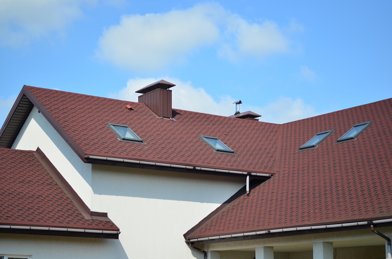 Modern Surprise residential house with a steep red asphalt shingle roof featuring multiple skylights and dormer vents under a bright blue sky.