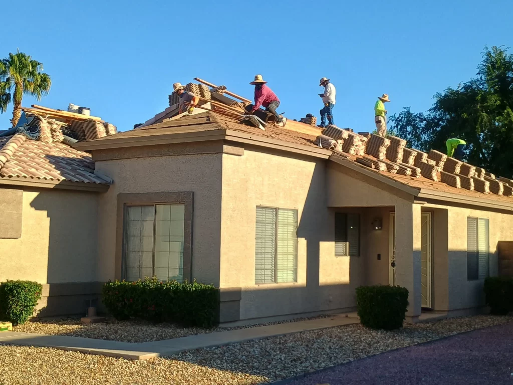 Crew of roofers in straw hats working on a tan stucco home, stacking and installing clay roof tiles during a clear sunny day in Arizona.